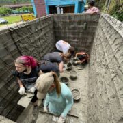 Students in Thailand lay bricks in a wall supervised by leaders