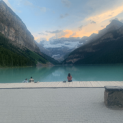 Image of a few people sitting by the water staring out at a scenic mountain view