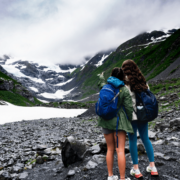 two students take a selfie in front of alaskan mountains