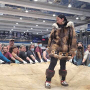 Speaker stands in the center of crowd wearing a fur coat in front of group of students