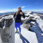 mackenzie stands on top of snowy mountain with blue sky behind her