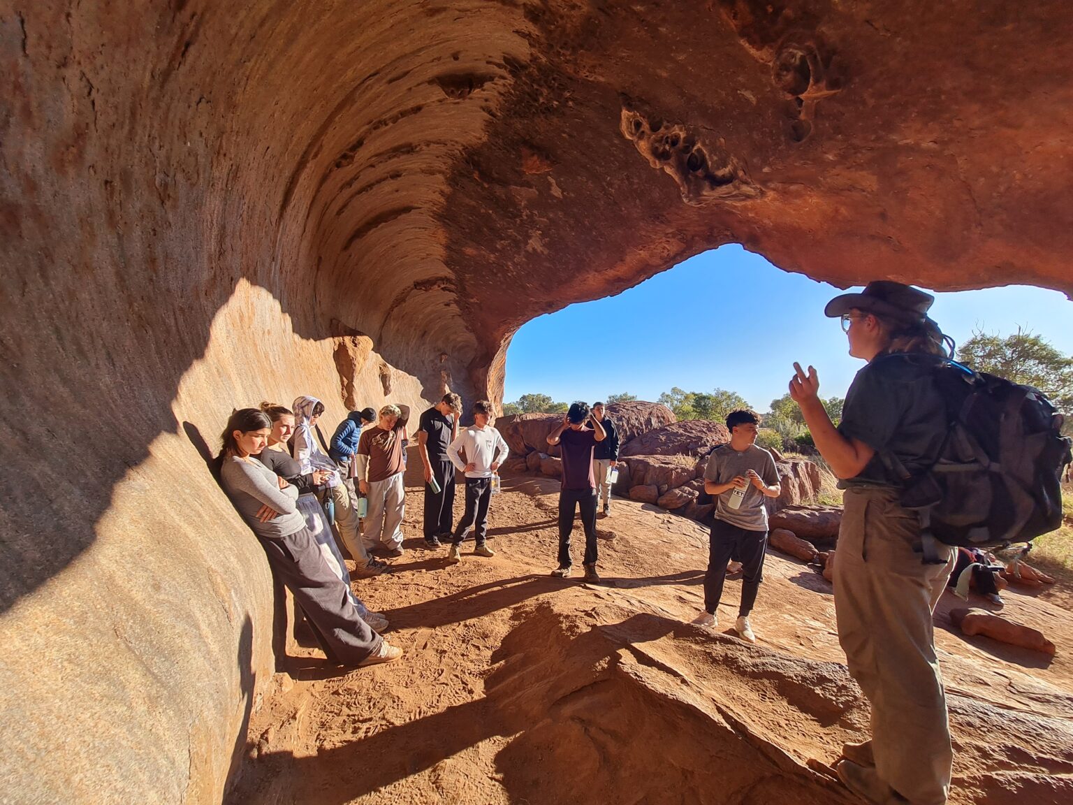 Students stand in natural cave listening to a local guide