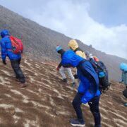 Students in colorful wind gear hike up rocky slope of Cotopaxi
