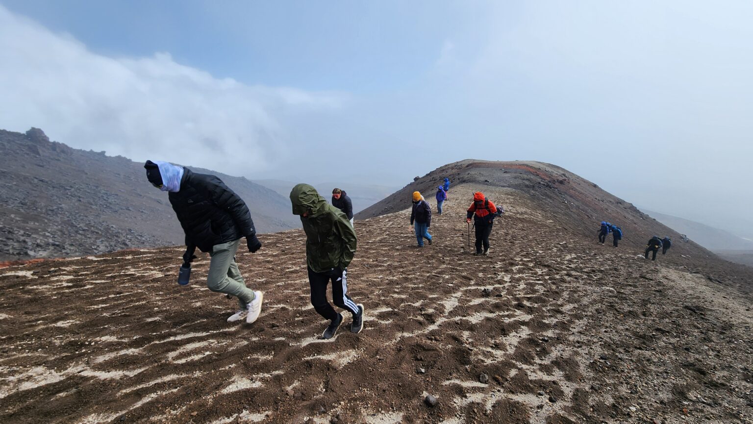 Students in colorful wind gear hike up rocky slope of Cotopaxi