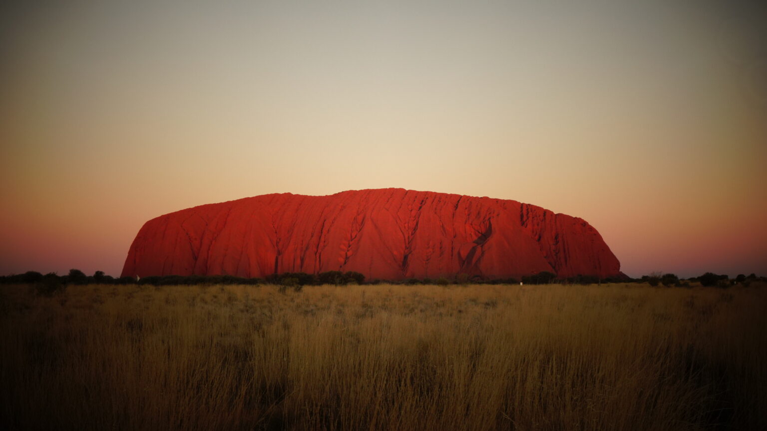 Red rock formation stands stark against clear sky and grass field 