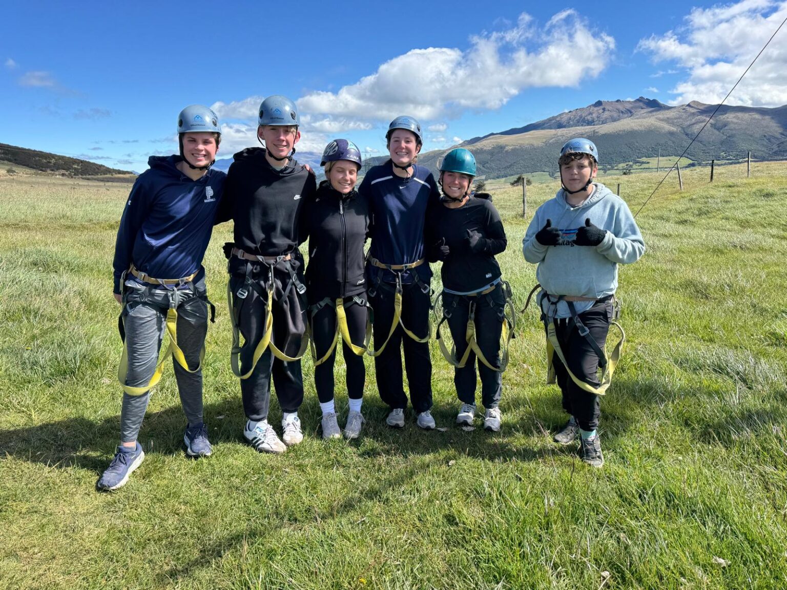 Students in helmets and straps stand pose a group photo outside