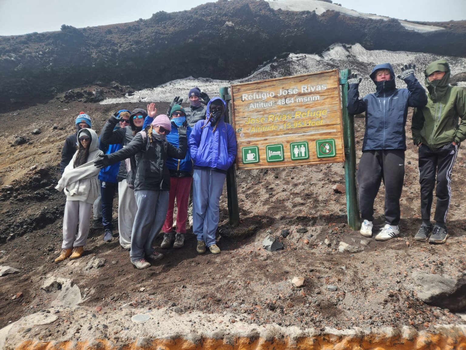 Student pose and cheer near sign that reads "San Jose Rivas Refuge"