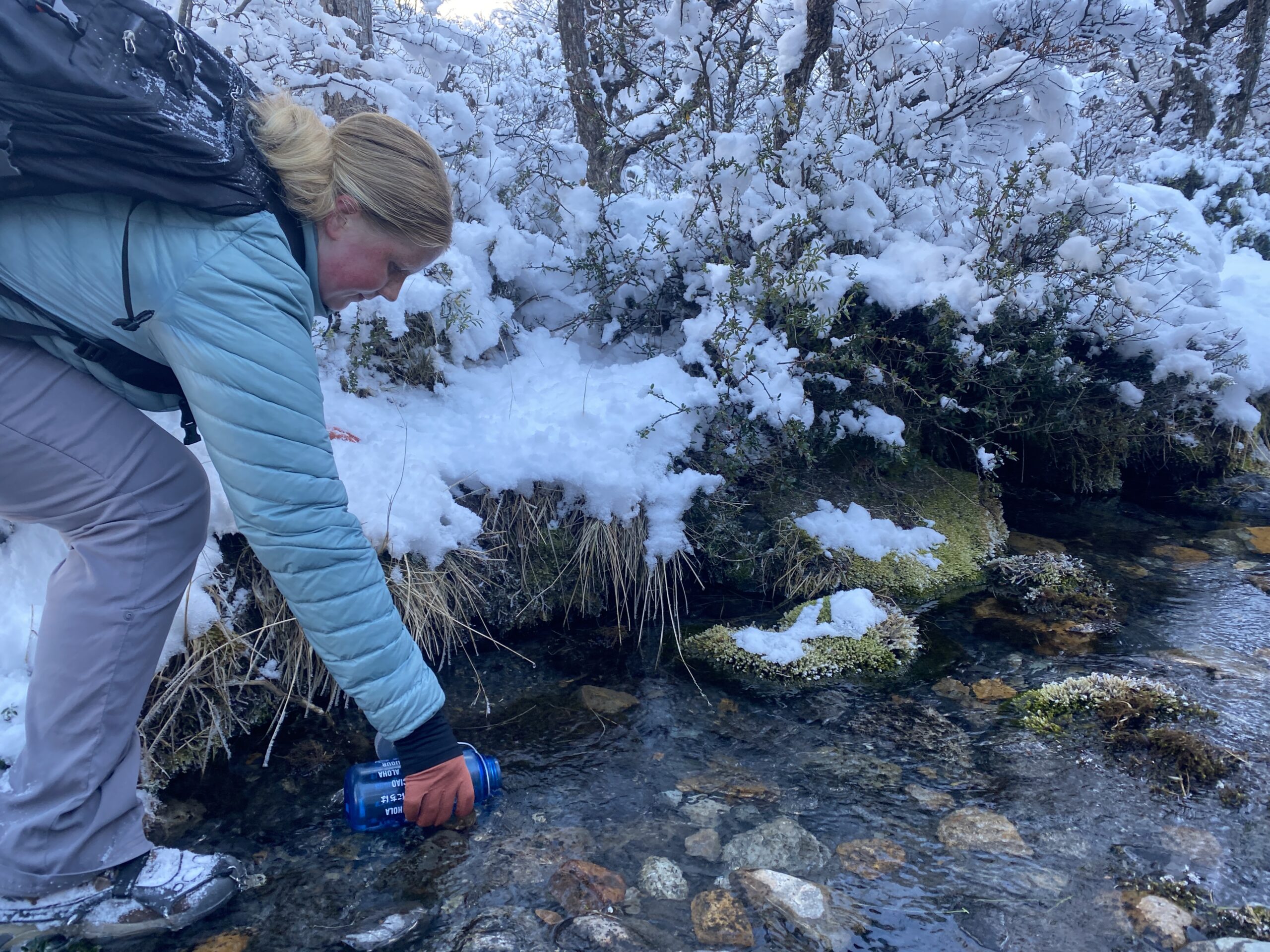 Student dips water bottle into fresh mountain river