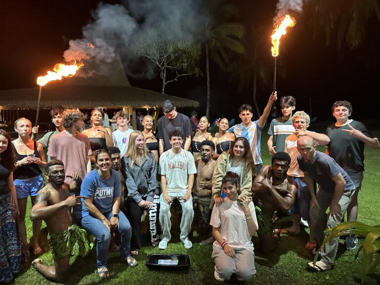 Students, two holding torches, pose for a group photo with Fijian locals.