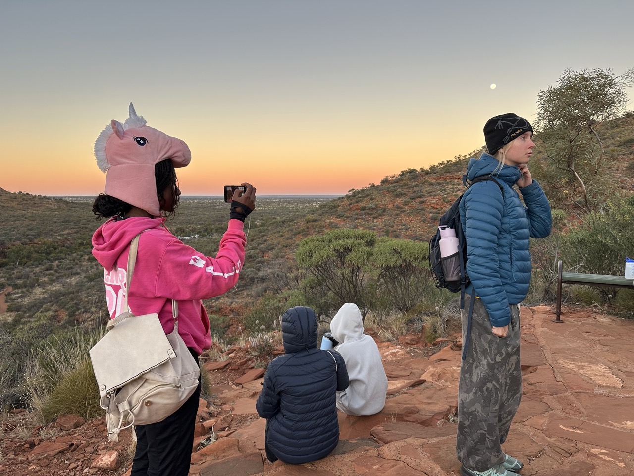 Students look out at sunset in the Outback, one wears a pink unicorn hat