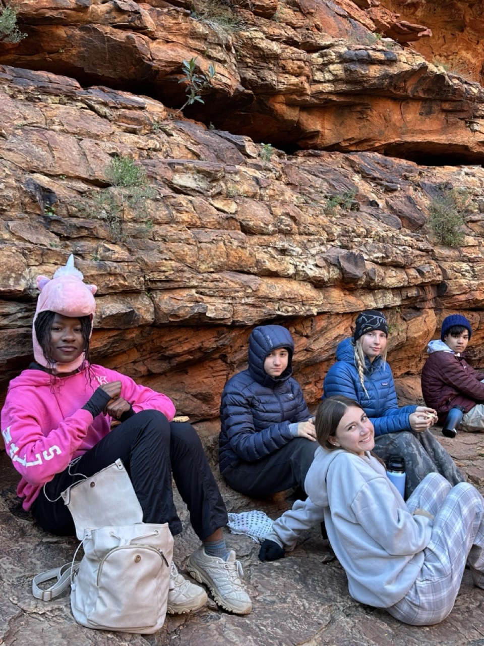Four student sit resting against red rocks 