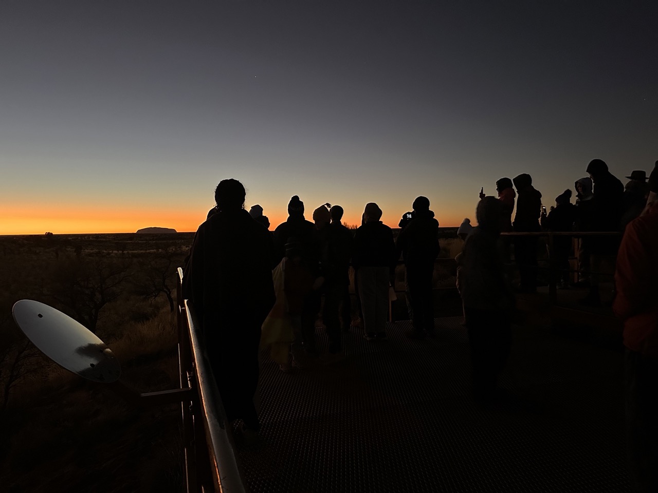 Figures of groups of students stand shadowed as sun almost completely sets