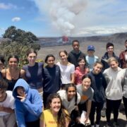 Students pose for a group photo in front of an exploding volcano