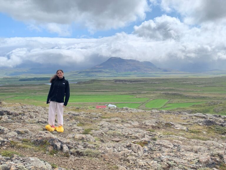 Student stands on rocks with Icelandic mountain range in distance behind
