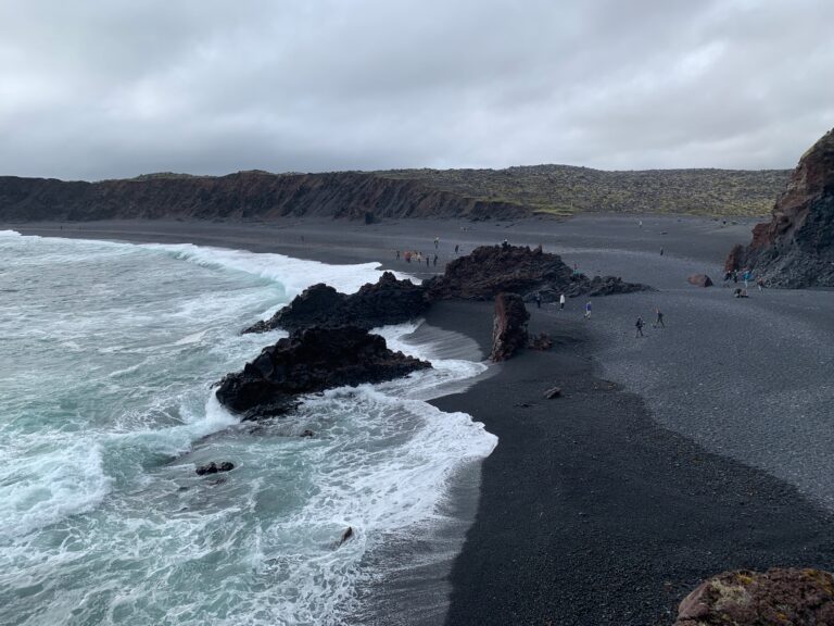 Bright blue waves crash on black sand beach