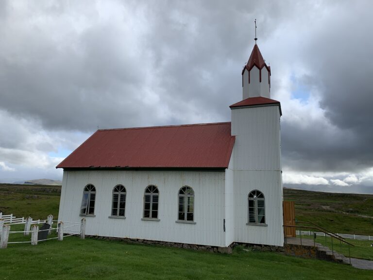 White church with red roof stands stark against cloudy gray sky