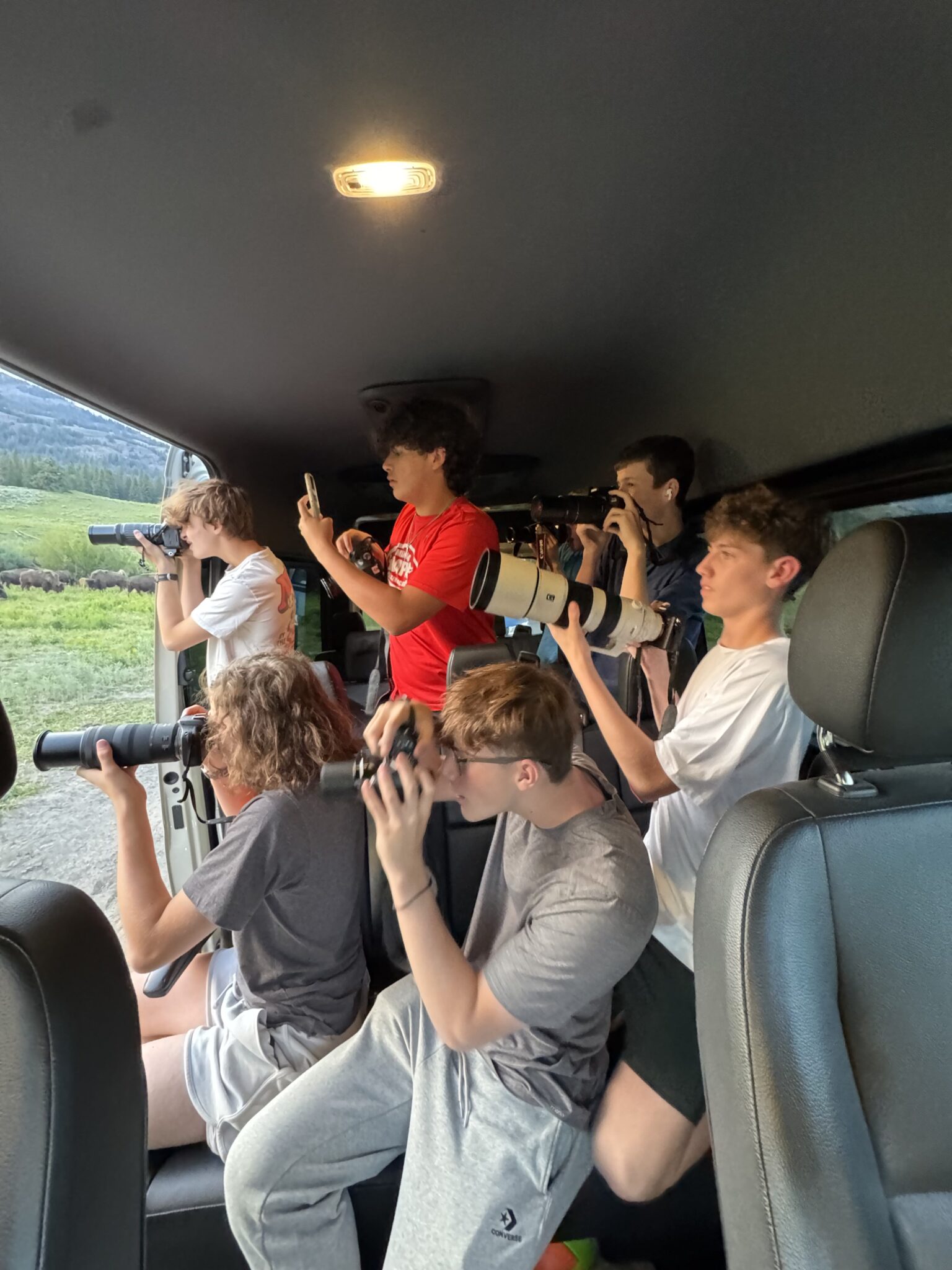 Six students in a van all hold up cameras taking photos of wildlife