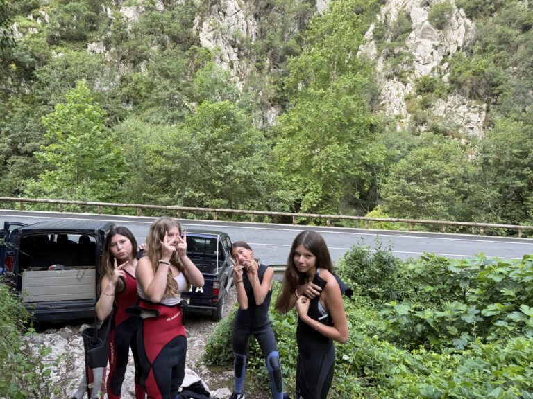 Four student stand near cars in the forest giving a thumbs up