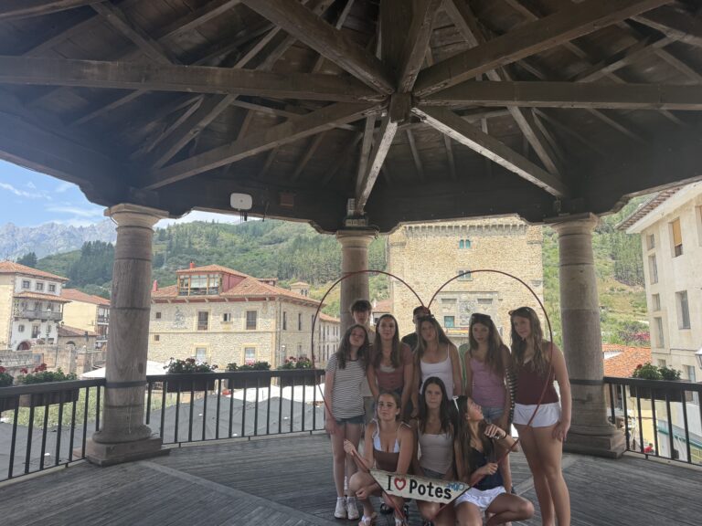 Students pose for a group photo in gazebo, one crouches down holding a sign that reads "I love Potes"