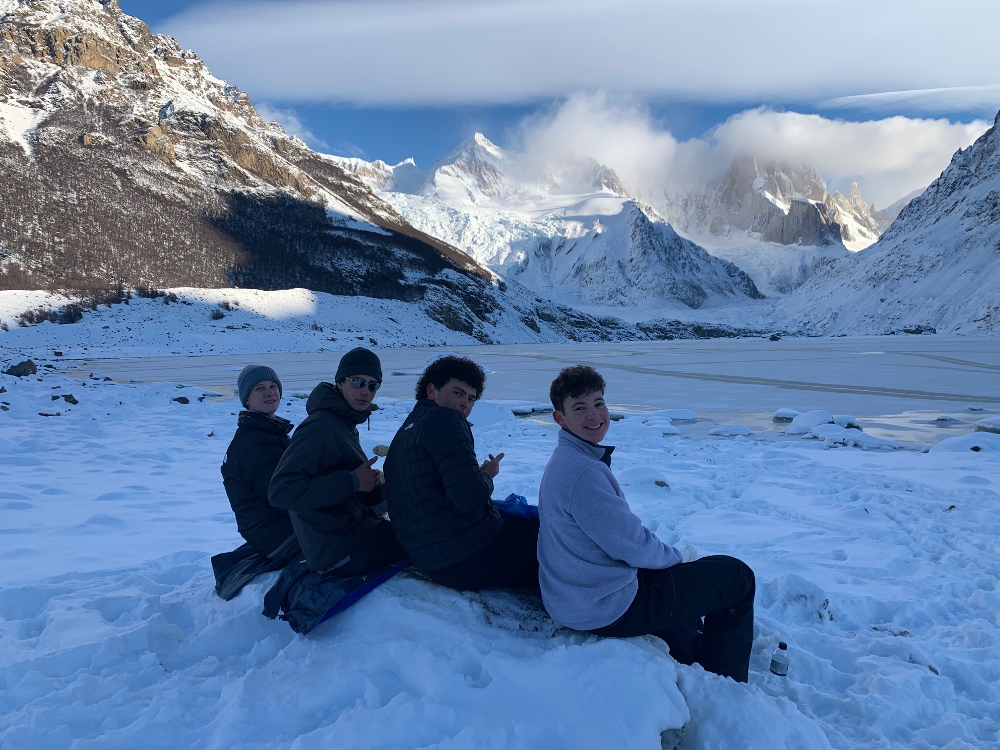 Students sit on snow mound looking out at frozen lake and Patagonian mountains
