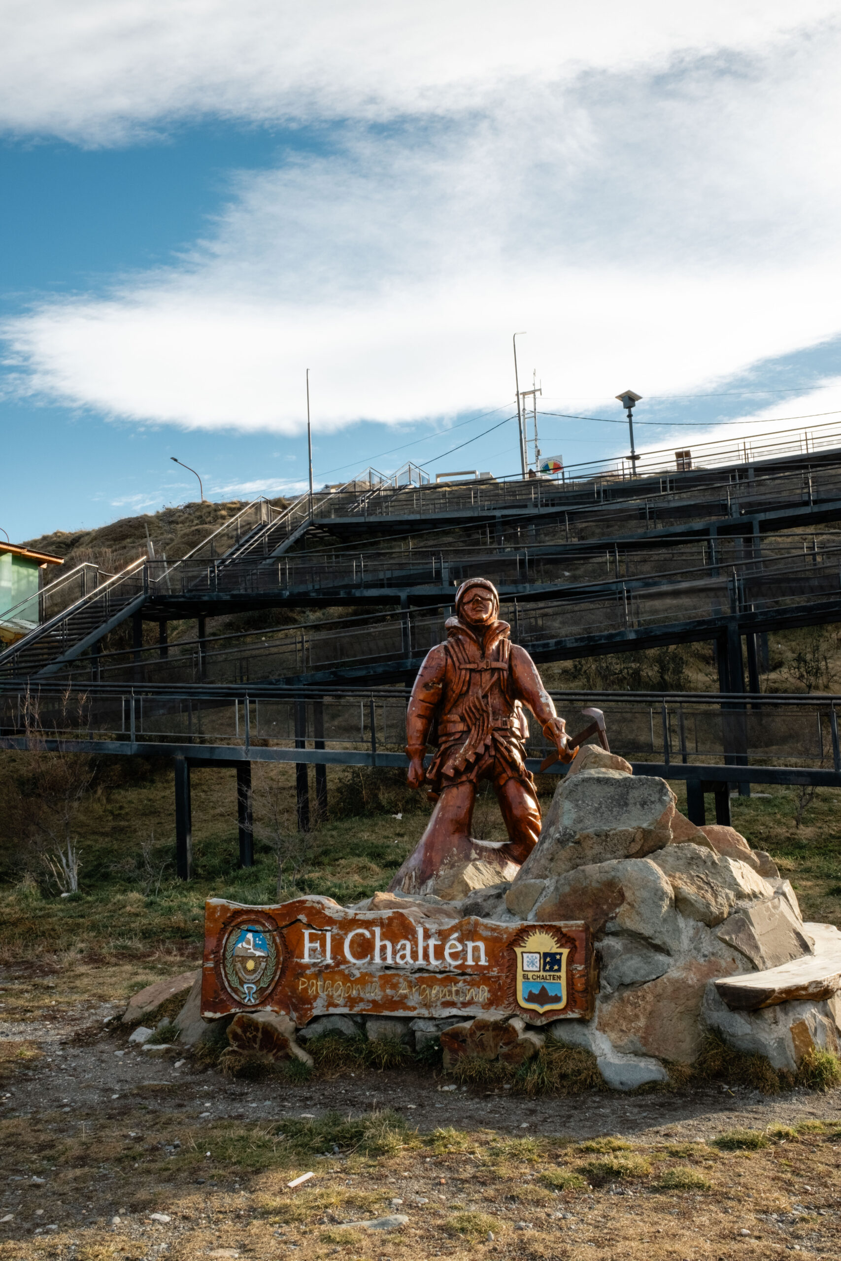 Statue of hiker in reddish bronze with sign under that reads "El Chaltén"