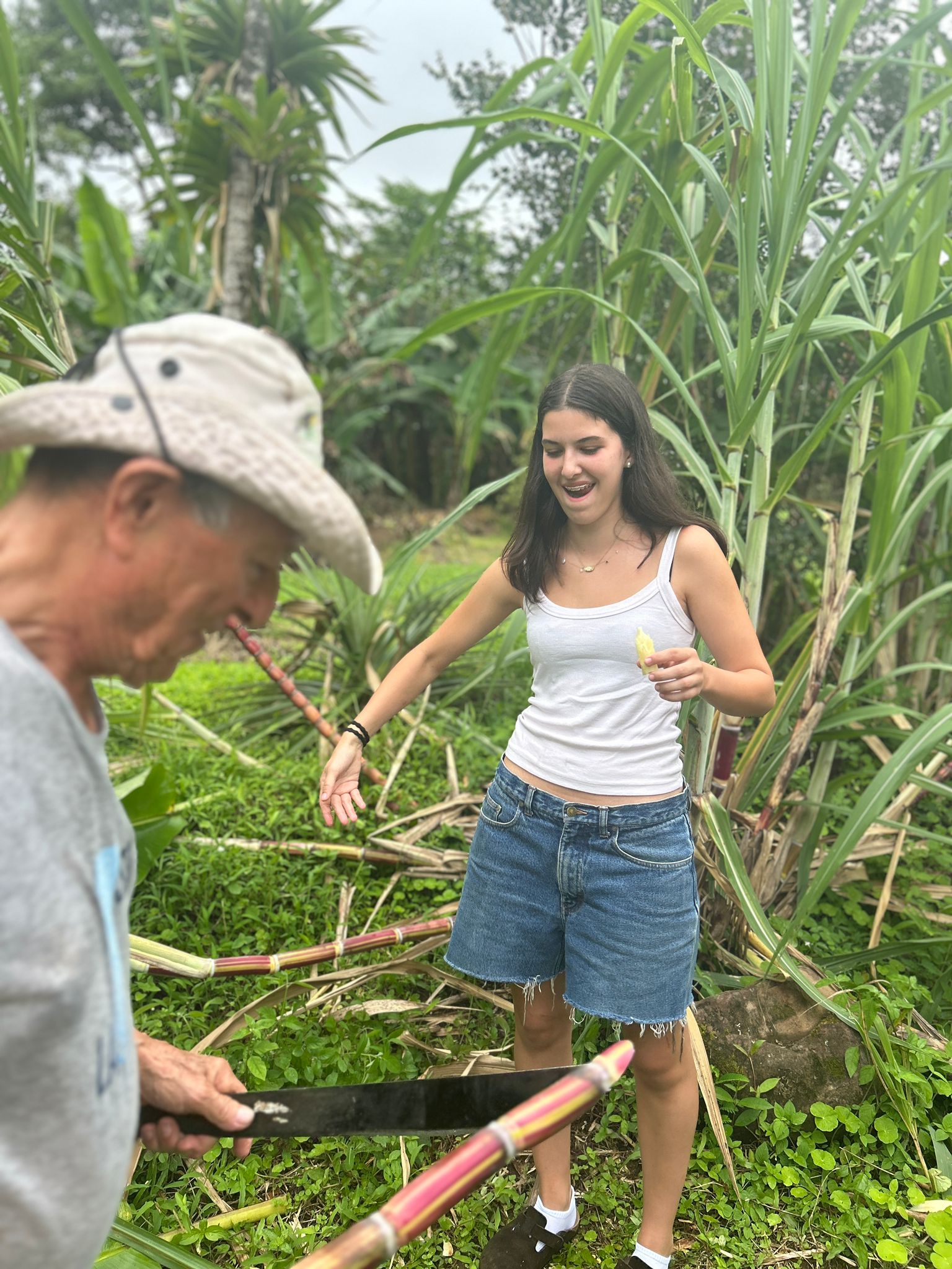 Student reacts excitedly as local instructor cuts sugarcane stalk with a metal blade