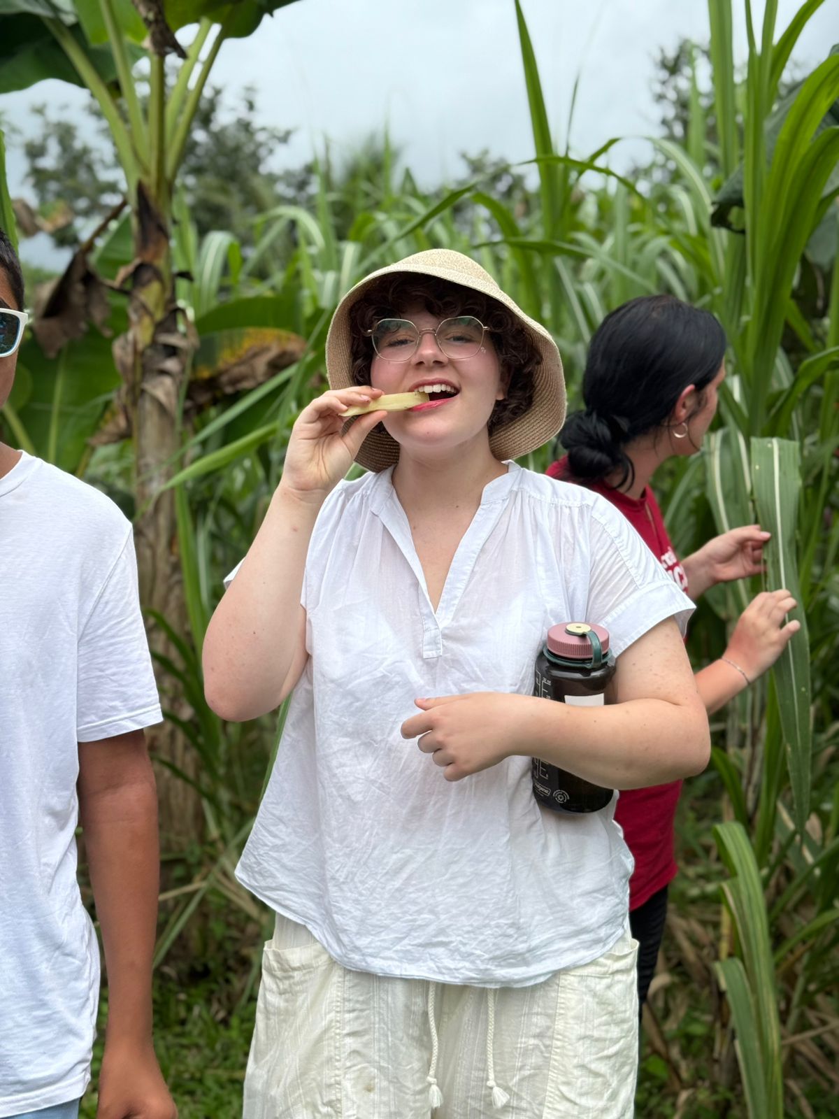 Student wearing a hat bites into a piece of fresh sugarcane