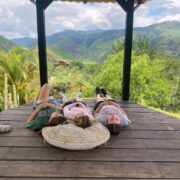 Three students lie on pillows in an outdoor pavilion, lush green mountains can be seen in the distance