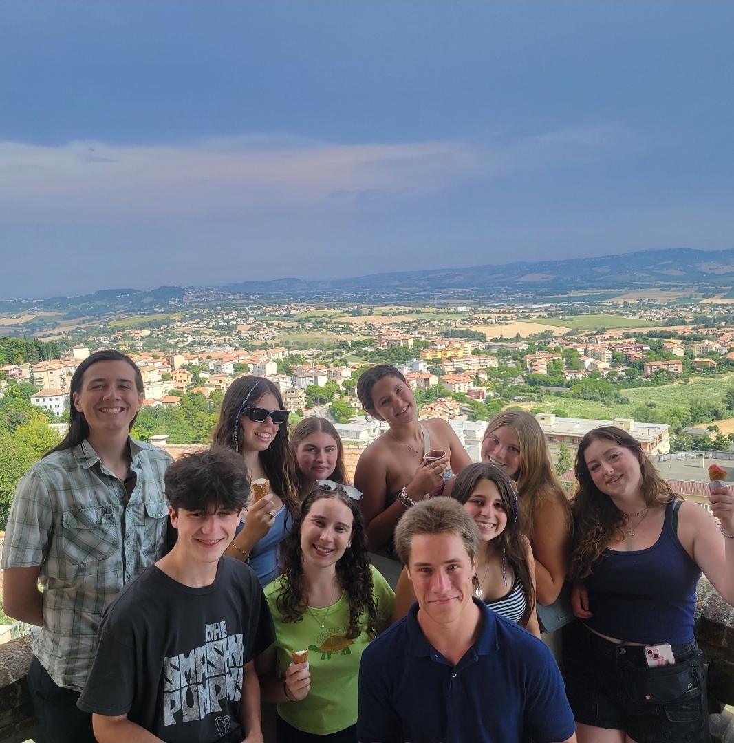 Group of student pose of picture with scenic landscape of rolling hills and homes in background in Osimo