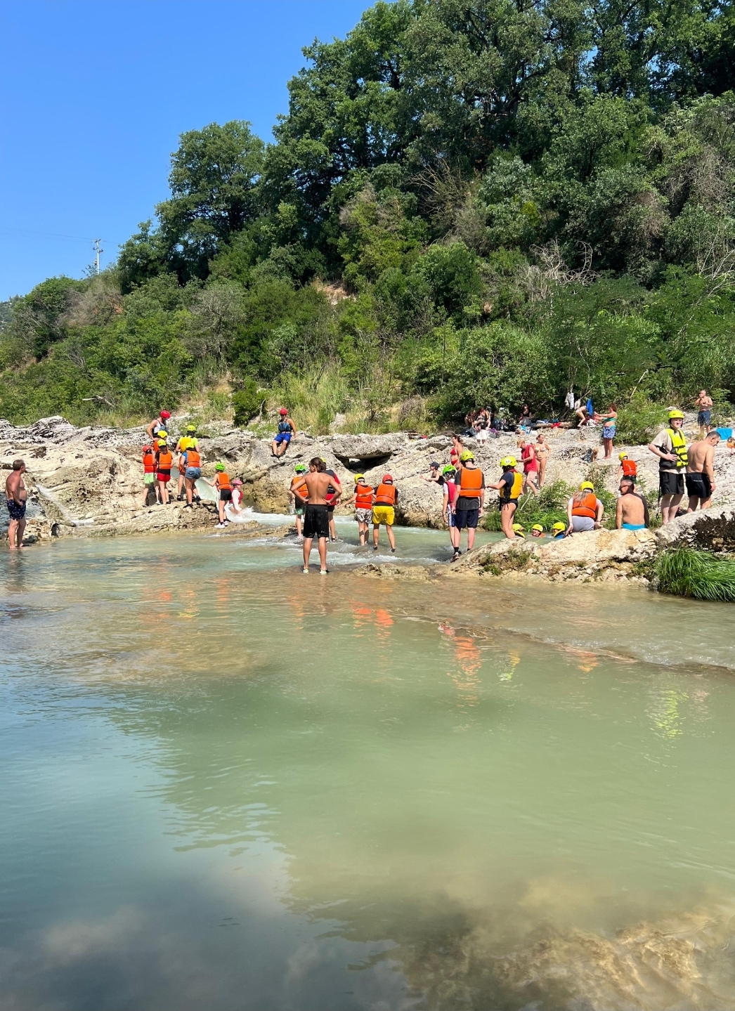 Students stand near natural pool of water on rocks wearing life vests and helmets