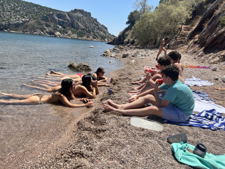 Students sit on a beach, some on the sand some half in the water