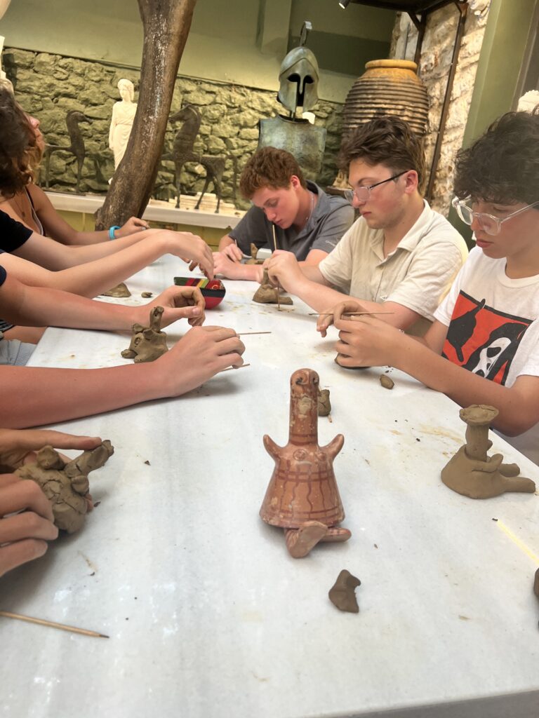 Students sit at a table molding clay dolls