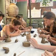 Students sit at table using their hands and sticks to mold clay
