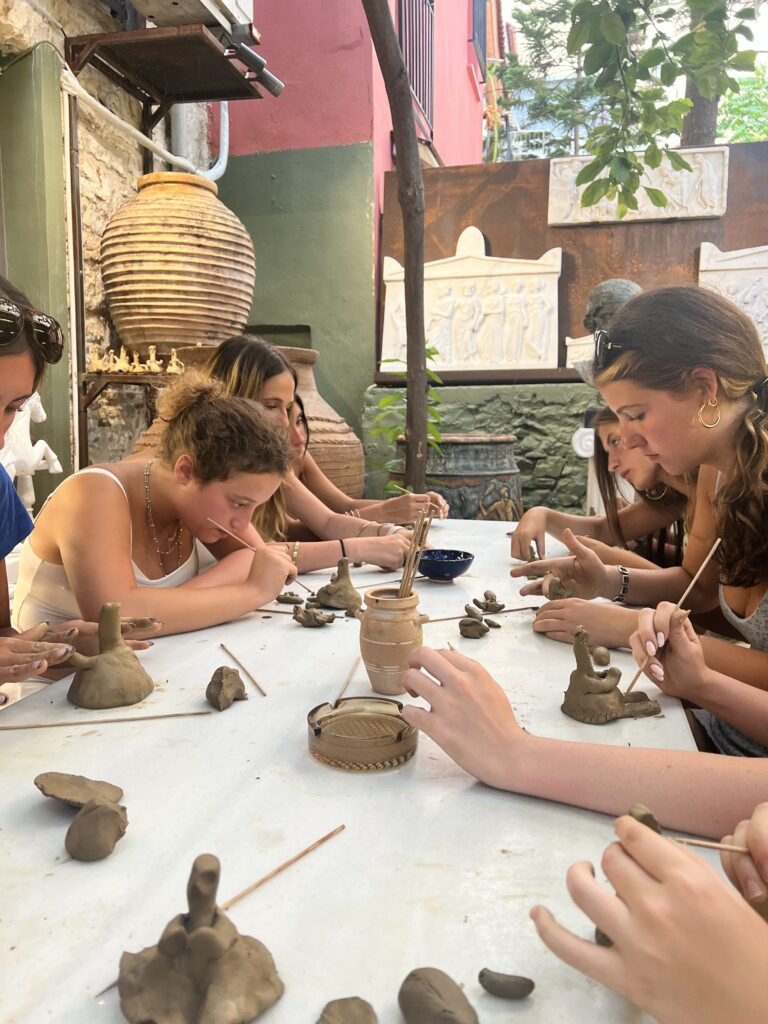 Students sit at table using their hands and sticks to mold clay 