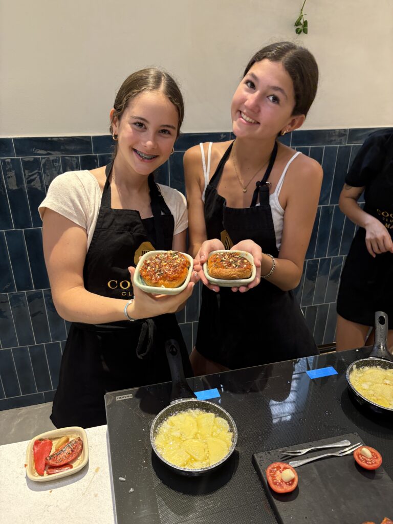 Two smiling students in black aprons hold up freshly made spanish tortillas 