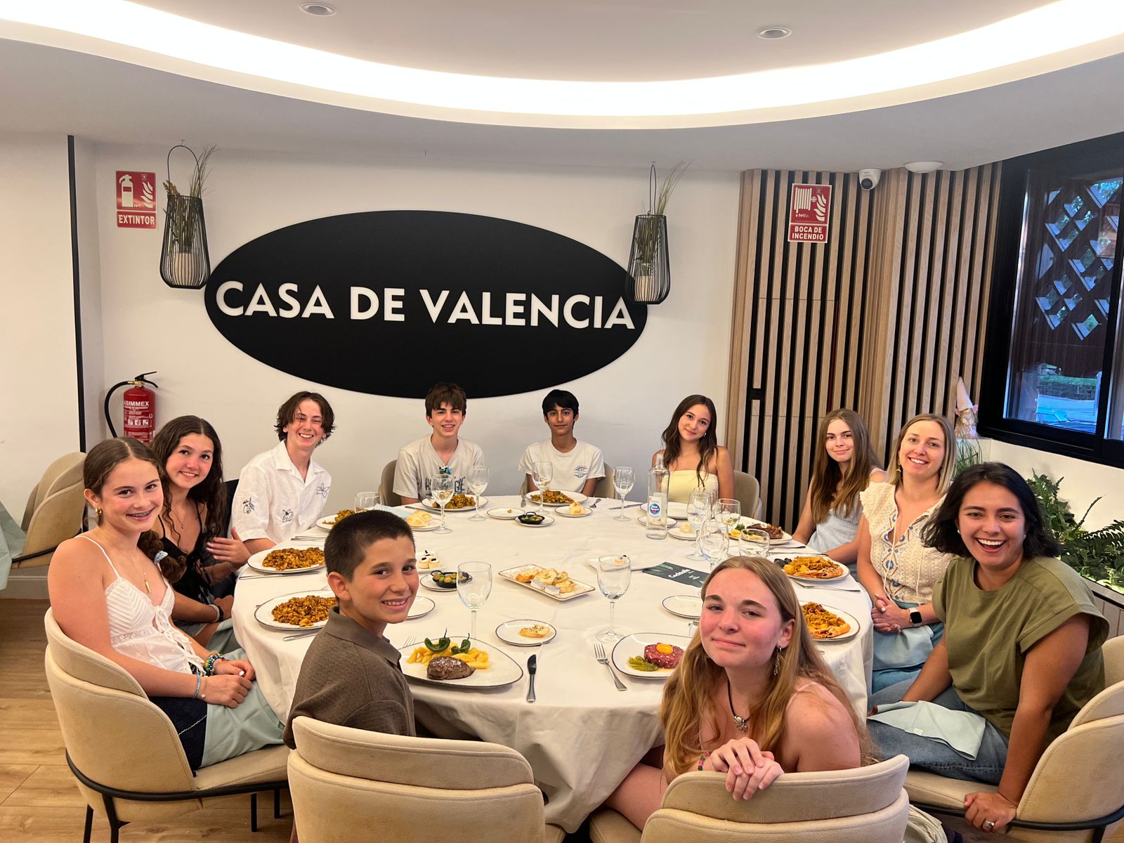Students sit a restaurant table with a sign behind them that reads "Casa de Valencia"