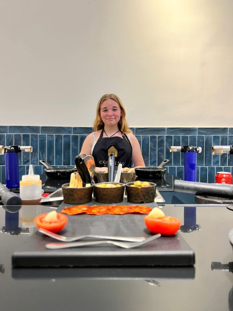 Student stands in kitchen with colorful ingredients and cooking tools laid out in front of her 