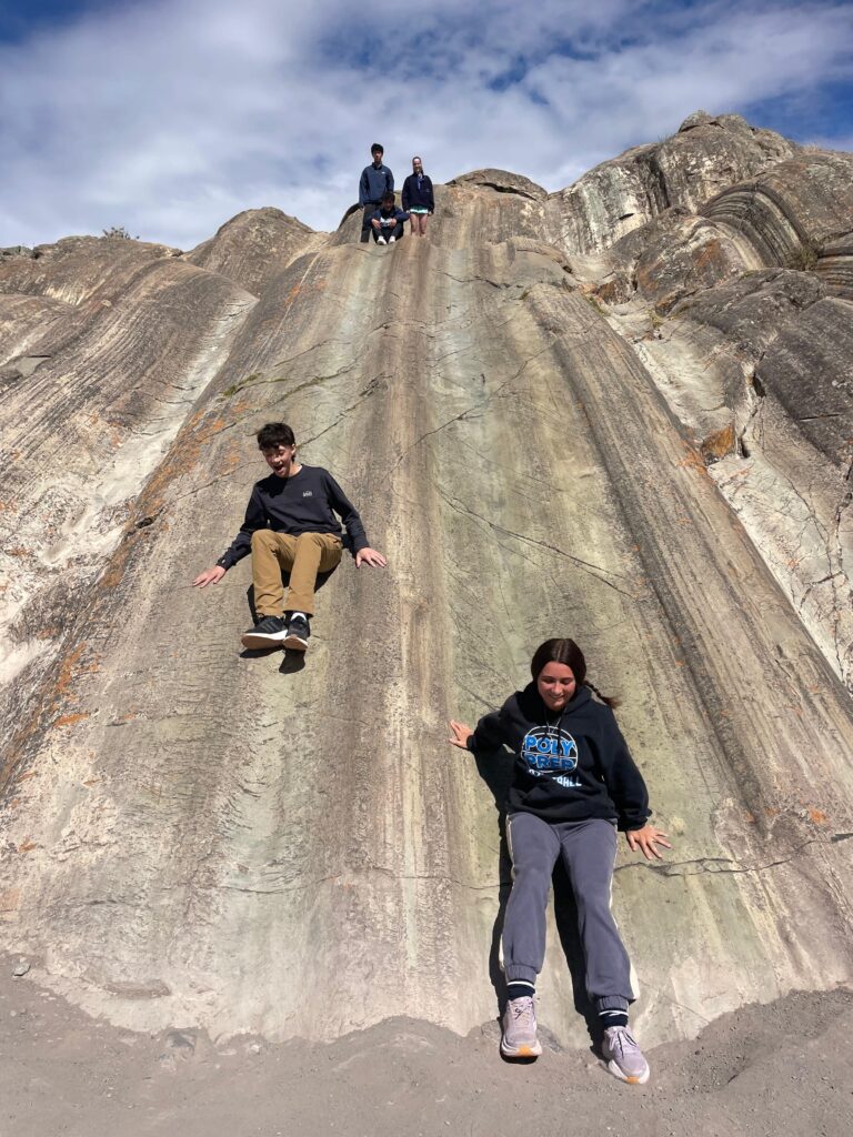 Two students slide down smooth rock face