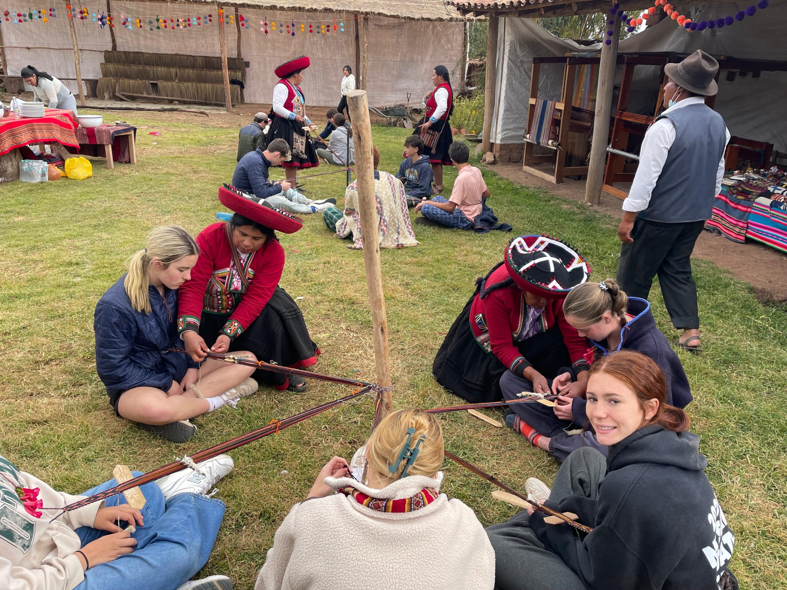 Four students sit outside learning to traditionally weave from a local leader
